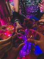 A group of friends raising glasses filled with bright, refreshing drinks under string lights.