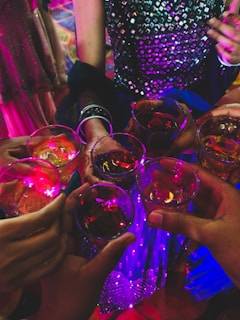 A vibrant crowd raising glasses in a joyful toast under warm string lights.