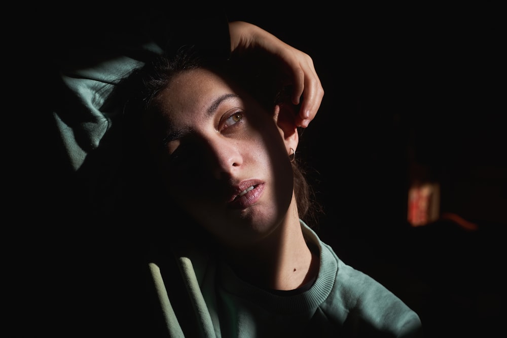 a woman is sitting in the dark with her hand on her head