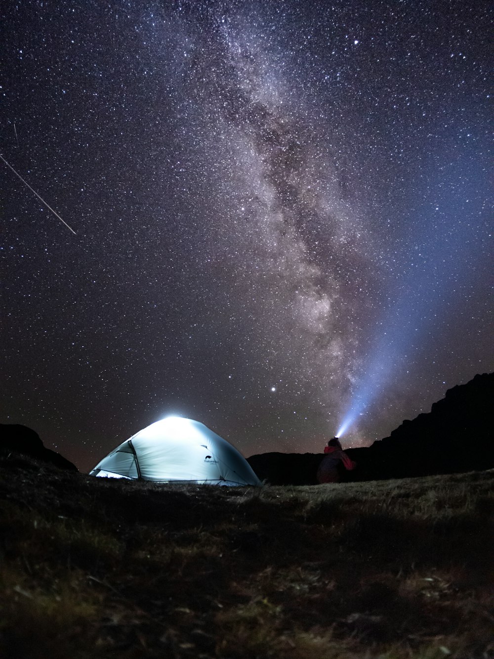 Una tienda de campaña en medio de un campo bajo un cielo nocturno lleno de estrellas