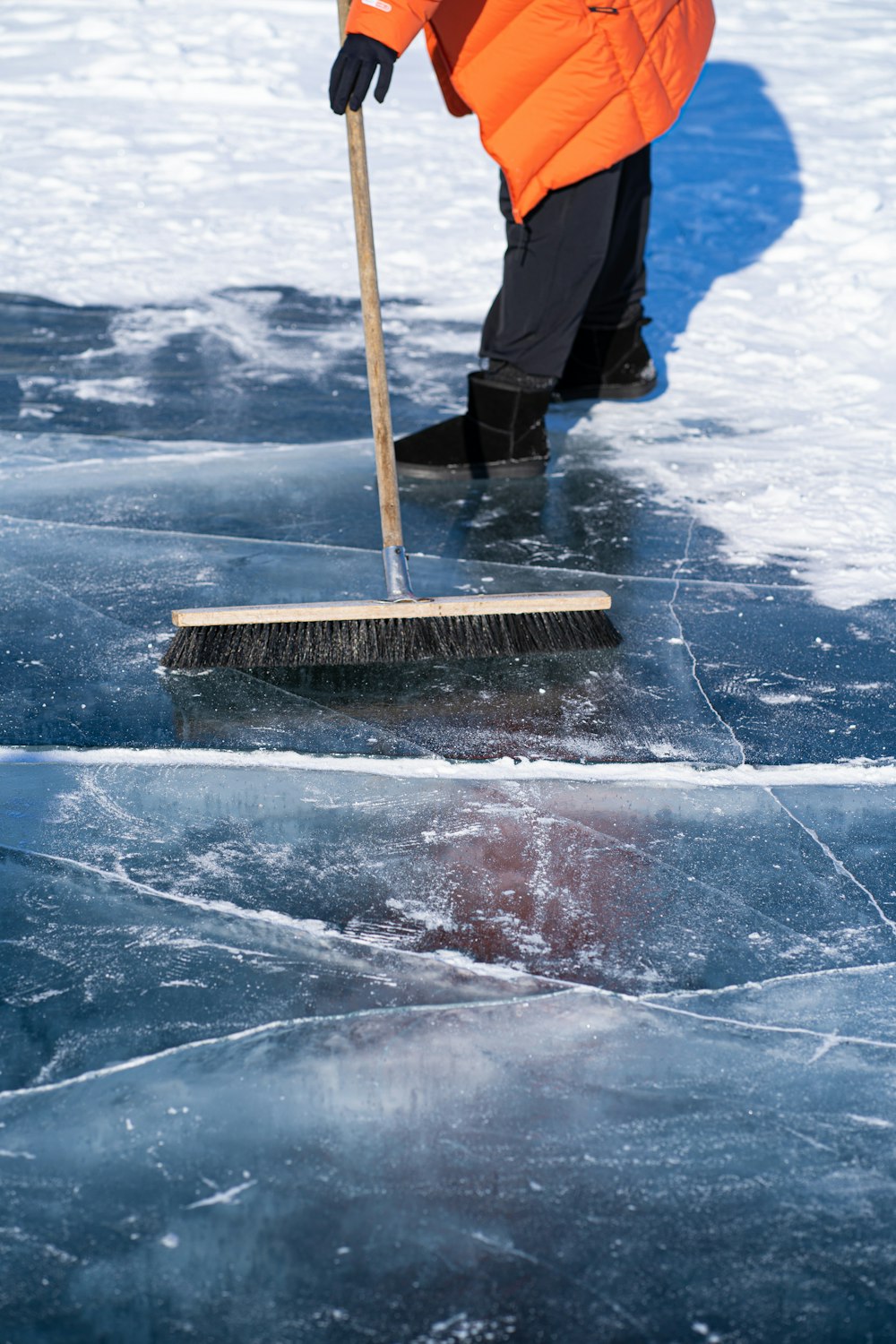 a person in an orange jacket is cleaning the ice with a broom