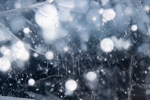 Frozen ice surface with trapped bubbles, exhibiting cracks and layers of varying clarity and opacity. The scene has a textured appearance with spherical air pockets scattered throughout.