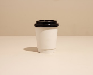 Minimalist silver-toned illustration of a coffee cup on a soft charcoal grey background.