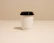 A close-up of a minimalist coffee cup on a white marble table with soft beige shadows.