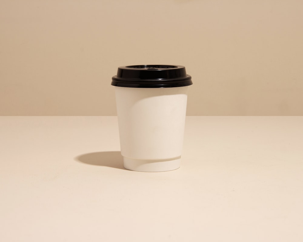 uma xícara de café branca com uma tampa preta