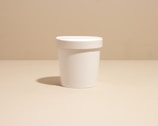 Plastic rigid pot container for cream with matching lid on a white background