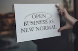 a person holding a sign that says open business as new normal