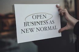 a person holding a sign that says open business as new normal