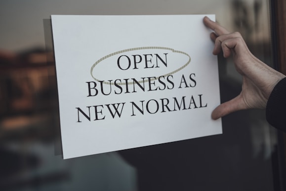 a person holding a sign that says open business as new normal