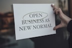 a person holding a sign that says open business as new normal