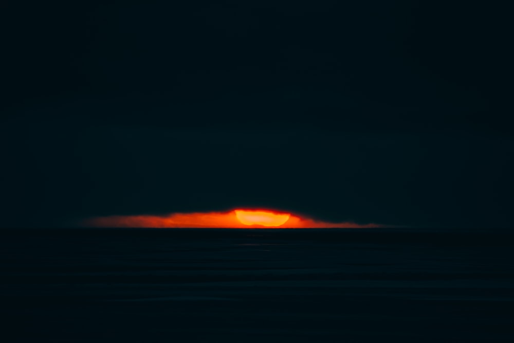 the sun is setting over the ocean in the dark