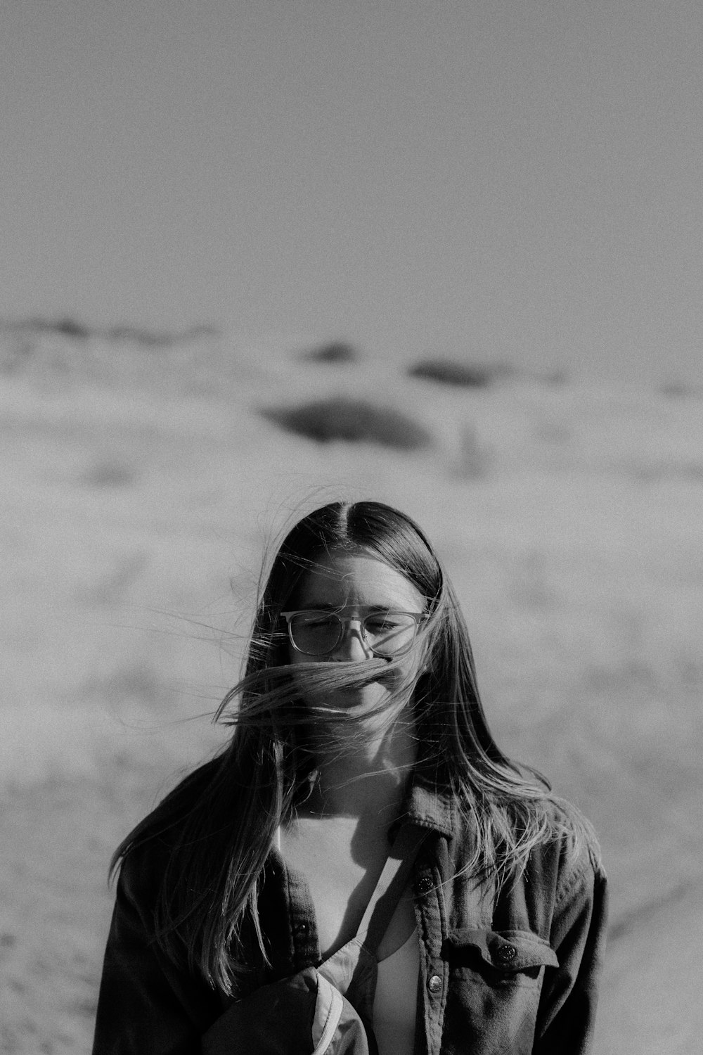 a woman standing on a beach with her hair blowing in the wind