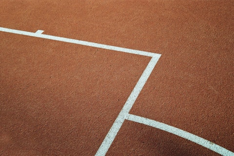 A section of a sports court with an orange textured surface and white painted lines forming a rectangle and part of a circle.