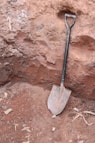a shovel stuck in the ground next to a rock