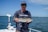 Fisherman holding a large fish on a boat during a sunny day at sea.