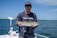 Fisherman holding a large fish on a boat during a sunny day at sea.