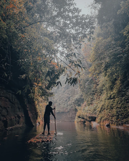 A person navigating a raft through a lively river surrounded by lush Indonesian jungle.
