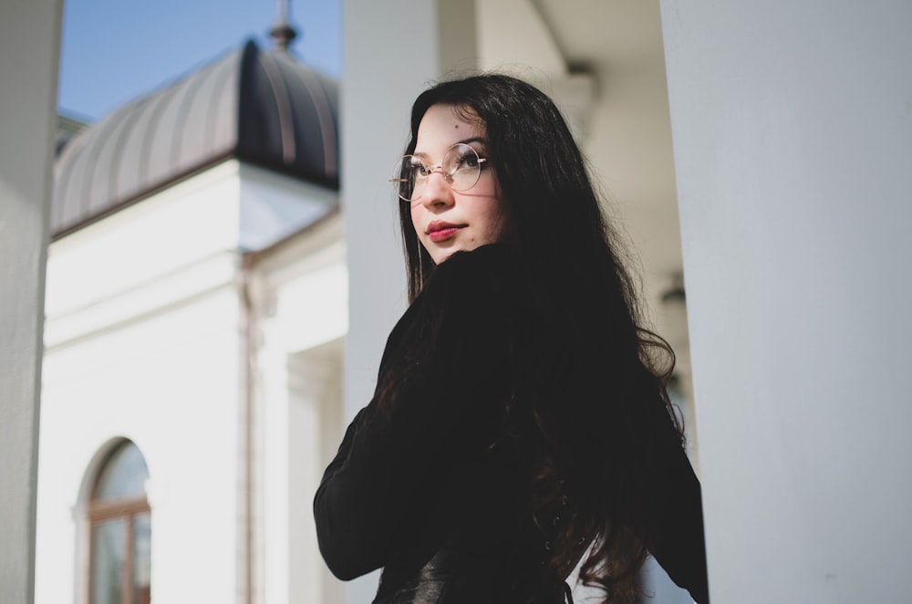 a woman wearing glasses standing in front of a building