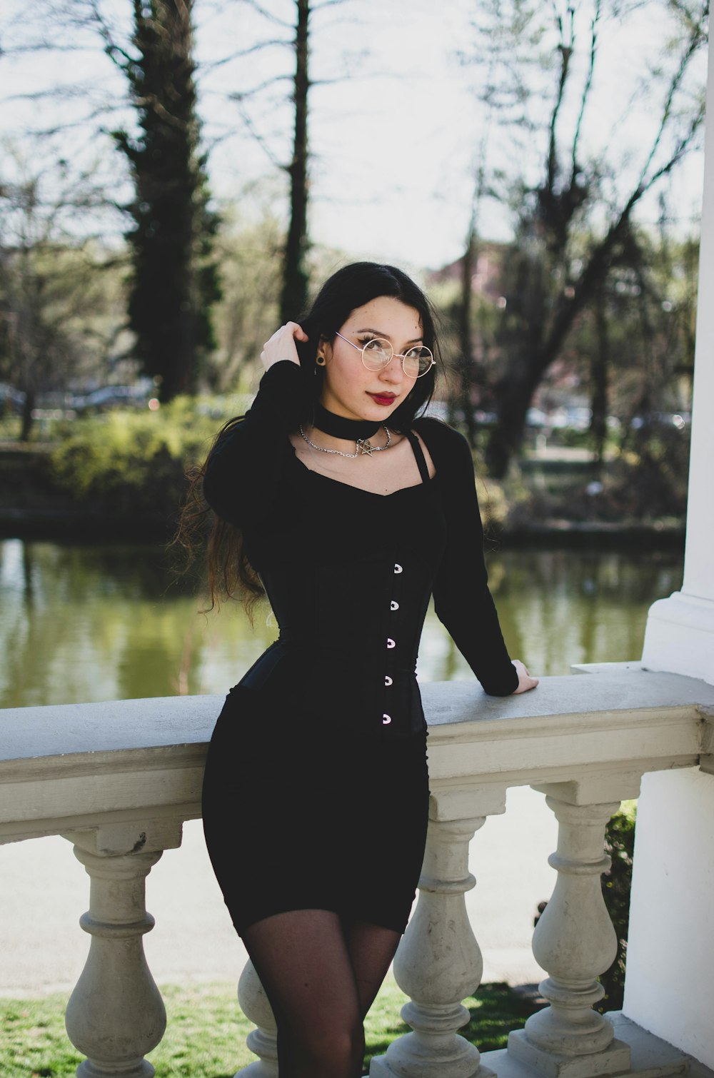 a woman in a black dress leaning on a fence