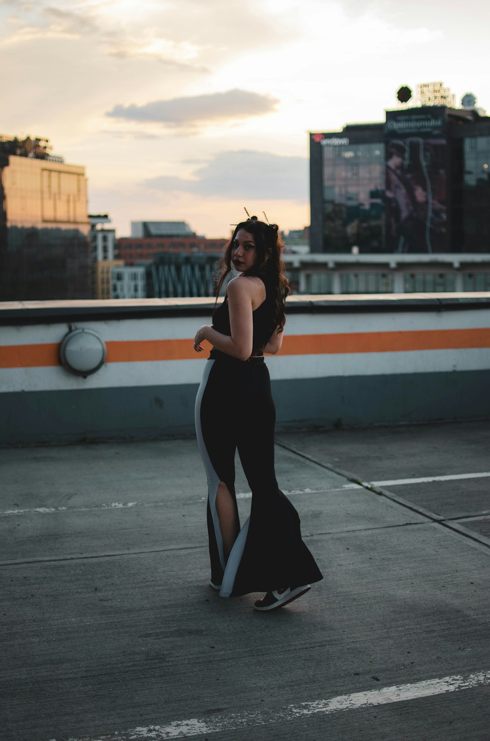 a woman in a black dress walking across a parking lot