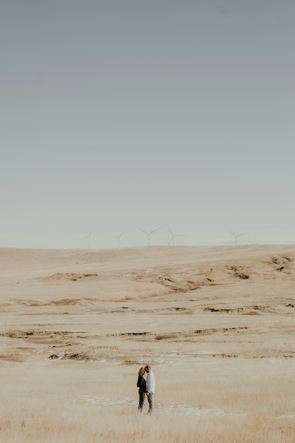 two people standing in a field with wind mills in the background