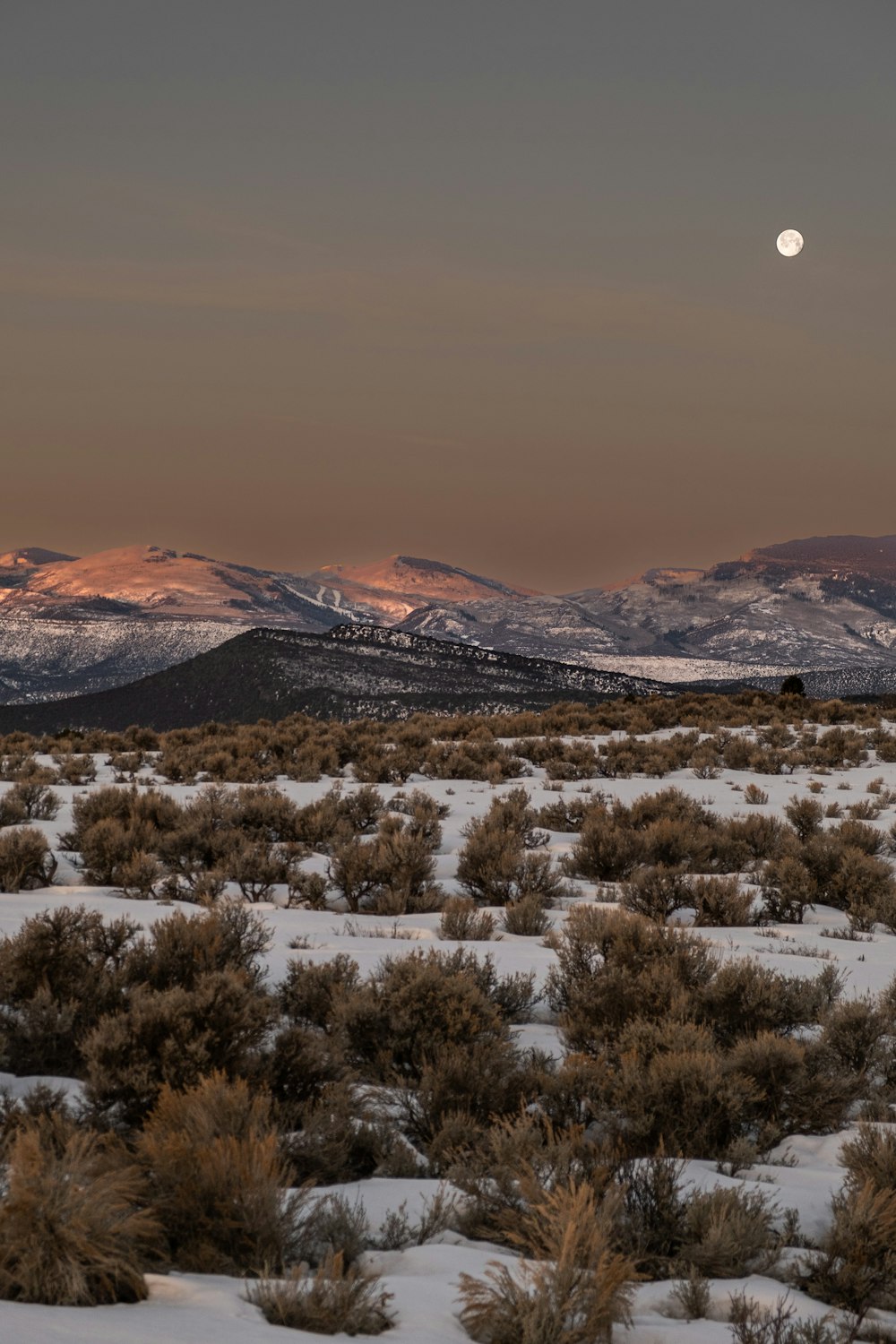 the moon is setting over the mountains in the desert