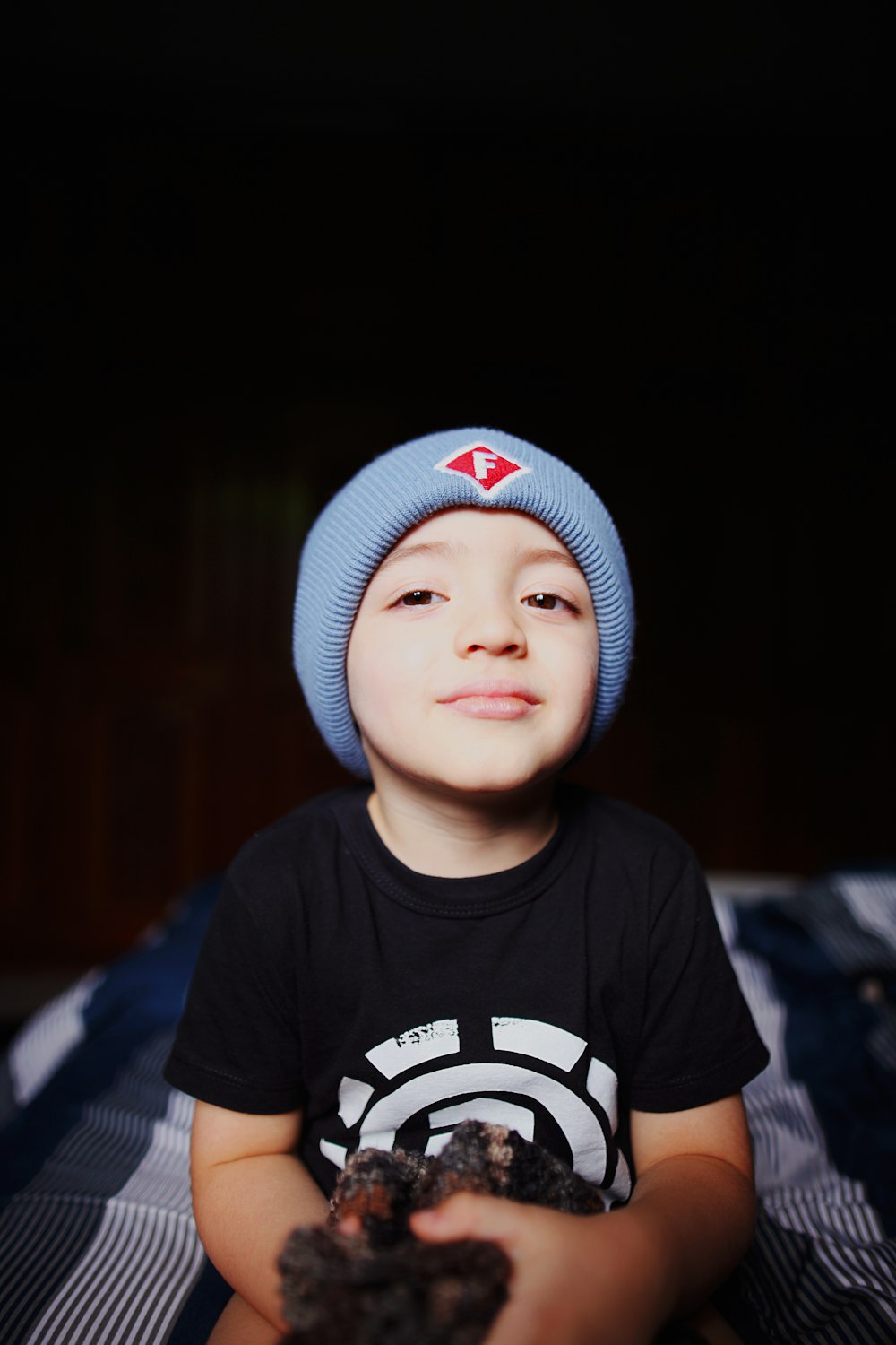 a young boy sitting on a bed holding a piece of food