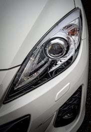 A close-up view of a car headlight showcasing the intricate design and reflective surfaces, surrounded by a glossy white exterior.
