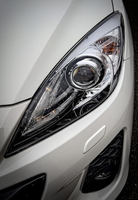 A close-up view of a car headlight showcasing the intricate design and reflective surfaces, surrounded by a glossy white exterior.