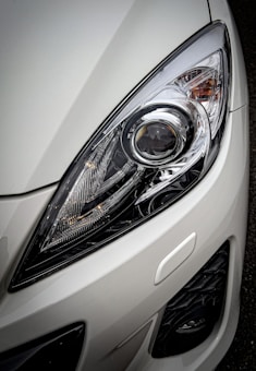 A close-up view of a car headlight showcasing the intricate design and reflective surfaces, surrounded by a glossy white exterior.