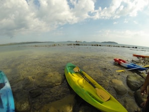 A kayak resting on a rocky shore with mountains rising in the background under a bright blue sky