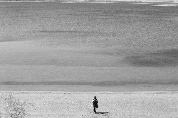 An emotional black-and-white photograph showing a solitary figure looking back towards a fading coastline, symbolizing both departure and hope.
