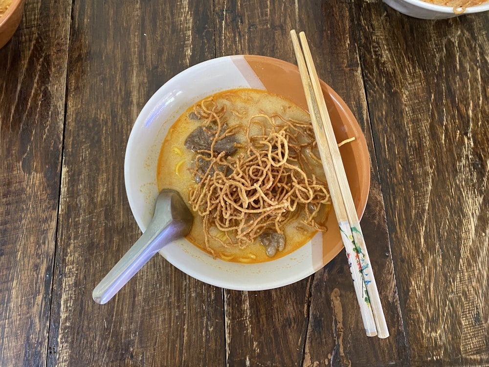 a bowl of noodles and chopsticks on a wooden table
