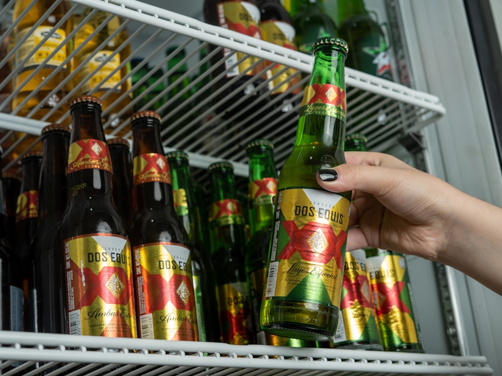 a person holding a beer in front of a refrigerator