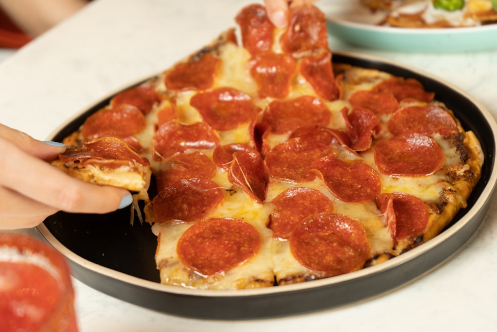 a person taking a slice of pepperoni pizza from a pan