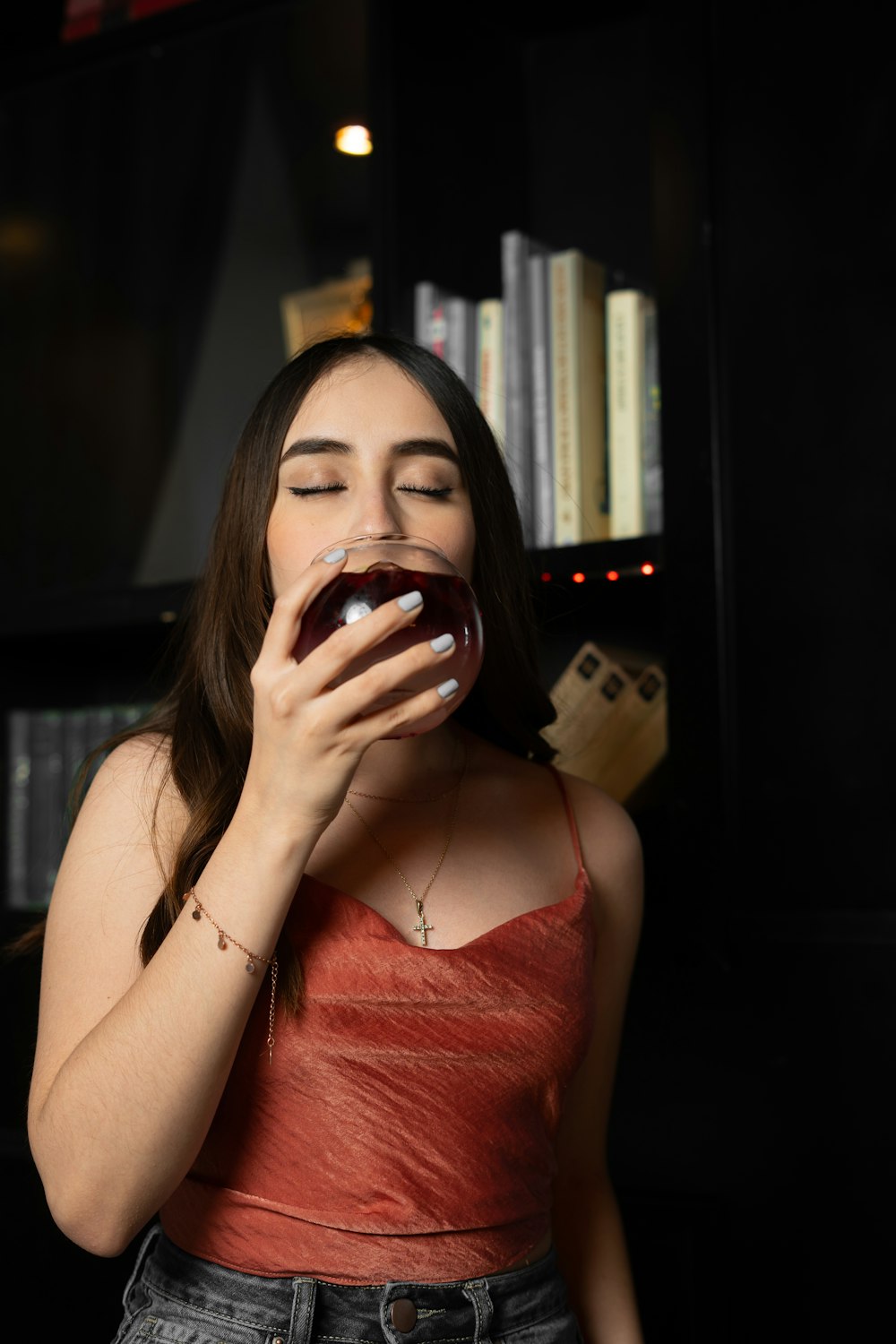 a woman drinking a glass of wine in front of a bookshelf