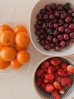 a bowl of cherries, a bowl of oranges and a bowl of straw