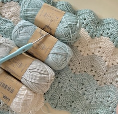 three balls of yarn and a crochet hook on a blanket