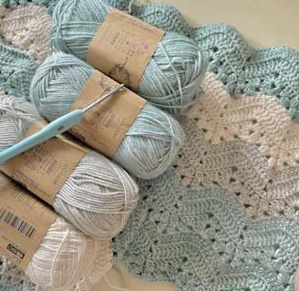 three balls of yarn and a crochet hook on a blanket