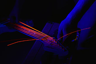 Close-up of a guitar neck being precisely adjusted with specialized tools under cyan and amber lighting.