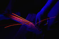 Close-up of a musician’s hands tuning a guitar under dim, electric blue stage lights.