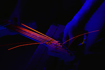 Close-up of a guitar neck being precisely adjusted with specialized tools under cyan and amber lighting.