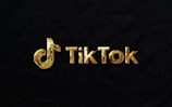 The image features a golden TikTok logo set against a dark, textured background.