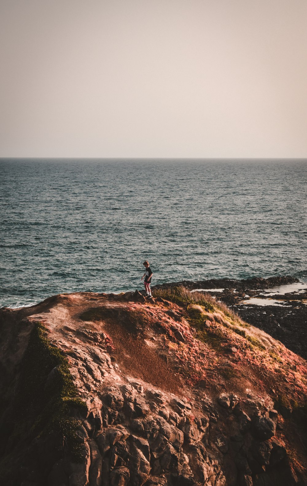 a man standing on top of a rocky cliff next to the ocean