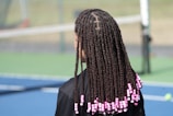 a woman with long box braids on a tennis court