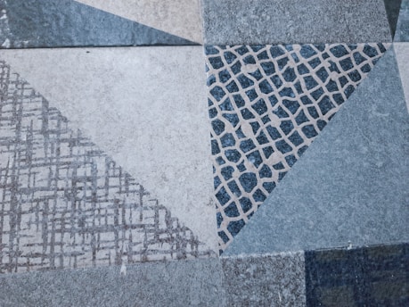 A geometric pattern featuring various triangular shapes with distinct textures and designs. The design includes a mix of linear grids and cobblestone-like patterns with a muted color palette.