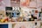 A collection of various figurines and small toys is arranged on a shelf. There's a Universal Studios clapperboard in the background along with colorful posters. The figurines include diverse characters from different media, arranged in a lively and eclectic manner.