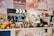 A collection of various figurines and small toys is arranged on a shelf. There's a Universal Studios clapperboard in the background along with colorful posters. The figurines include diverse characters from different media, arranged in a lively and eclectic manner.