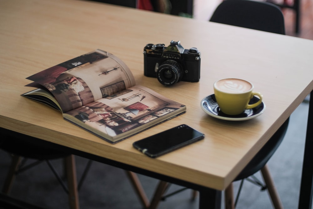 a table with a coffee cup, camera, cell phone and magazine on it