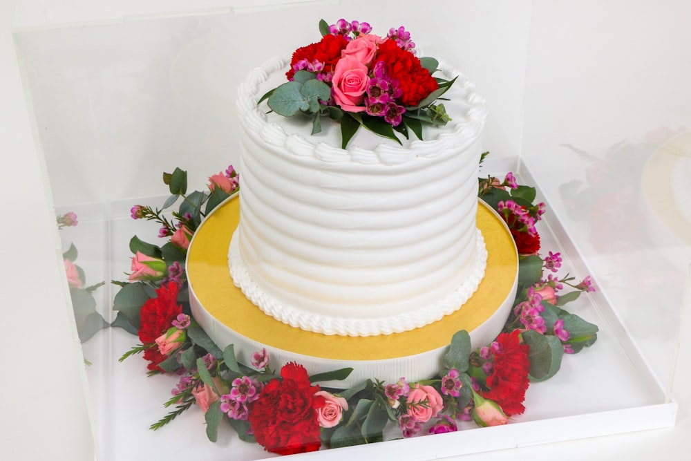 a three tiered white wedding cake with red and pink flowers
